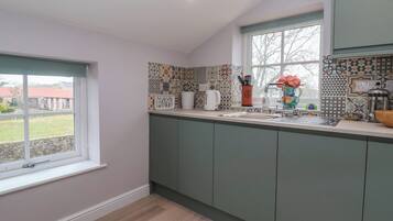 Una cocina moderna con armarios verdes, un ventanal grande y azulejos decorativos en la pared.