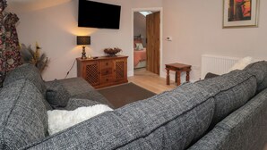 A living room with a sofa, a TV mounted on the wall, a wooden cabinet, and a painting on the wall. - The Hayloft (Richmond)