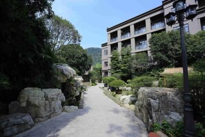 A pathway leading to a building with multiple balconies, surrounded by greenery and stone structures. - Tabao Garden (Chongqing)