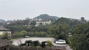 A parking lot with a white car, surrounded by trees and buildings on a hill.