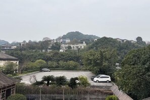A parking lot with a white car, surrounded by trees and buildings on a hill. - Tabao Garden (Chongqing)