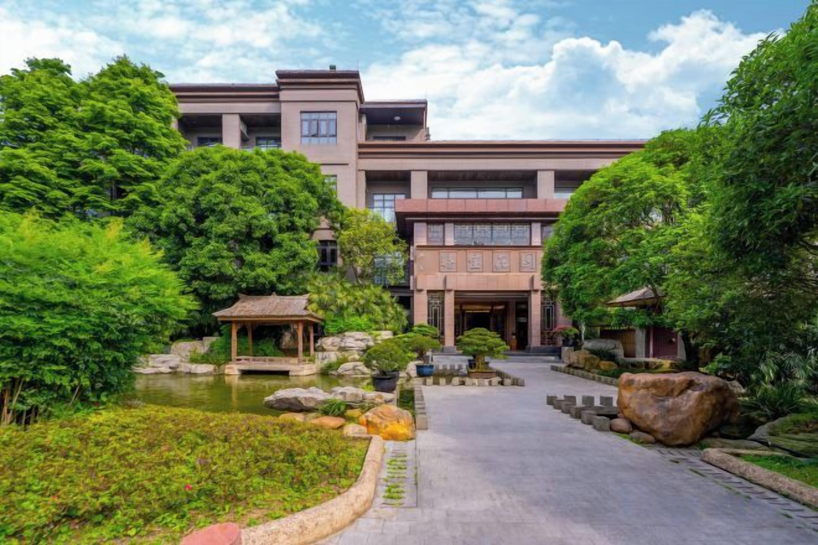 A building with a traditional architectural style, surrounded by lush greenery and a small pond.