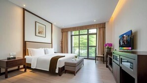 A hotel room with a large bed, a bedside table, a small table with a plant, a view of greenery through the window, and a kitchen area with a microwave. - Tabao Garden (Chongqing)
