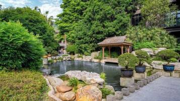 Un jardin paisible avec un étang, un kiosque et diverses plantes en pot.
