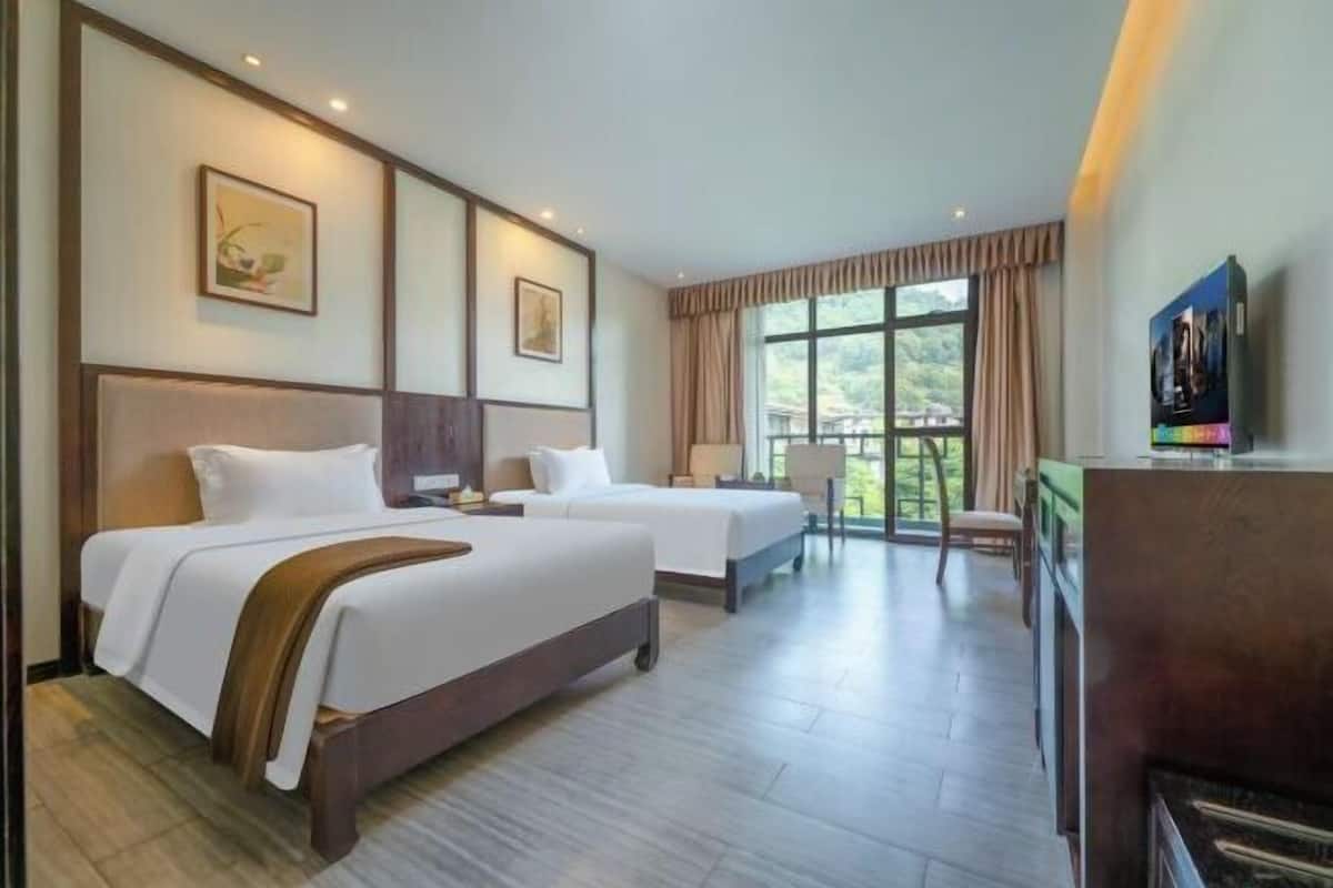A hotel room with two beds, a TV, a desk, and a view of the outdoors.