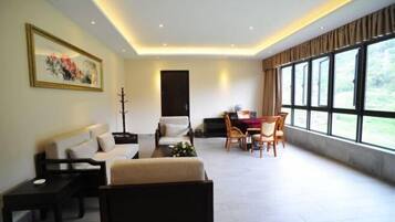 Ein modernes Wohnzimmer mit einer Couch, einem Esstisch mit Stühlen und einem großen Fenster mit Blick auf Grünflächen.