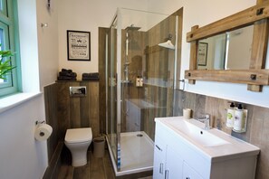 Um banheiro moderno com box de vidro, vaso sanitário branco e toucador com espelho.