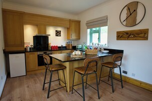 Una cocina moderna con armarios de madera, una isla central con taburetes altos, un horno empotrado y un reloj de pared.