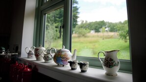 A window sill with various ceramic teapots and cups, a red mug, and a view of a green field through the window. - Tring Grange Cottage - Sleeps 2 - Onsite Parking (Tring)