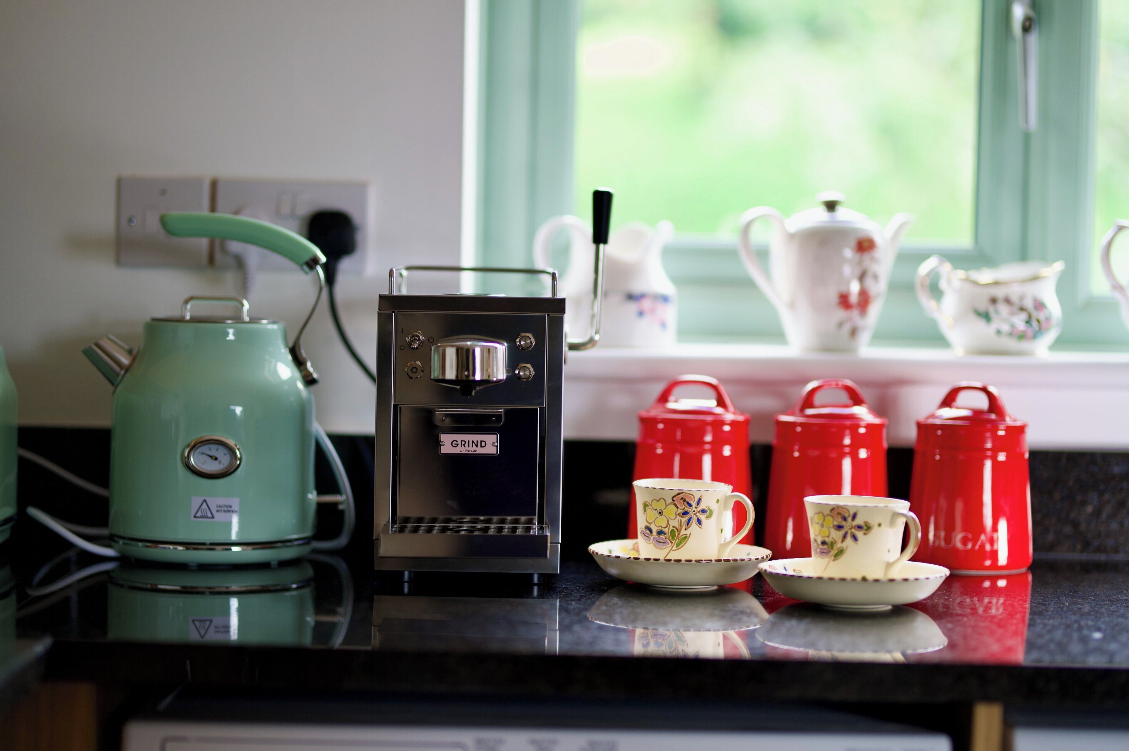 A kitchen counter with a coffee maker, a grinder, and a set of teapots and cups.