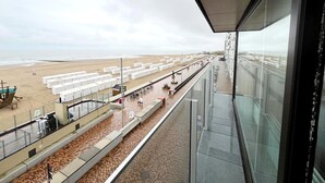 Udsigt over stranden og havet fra en balkon med gelænder i glas.