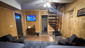 A room with wooden walls, a TV mounted on the wall, a staircase, and two beds. - Trailhead Riverfront Cabin (McCarr)