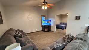 A living room with a gray sofa, a television, a ceiling fan, and a fireplace. - Trailhead Riverfront Cabin (McCarr)