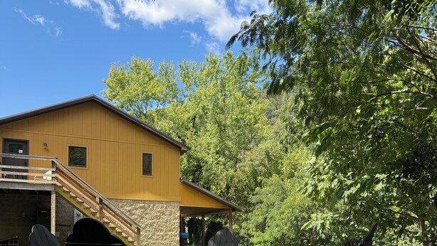 A yellow building with a wooden deck and outdoor seating area including Adirondack chairs and a fire pit. - Trailhead Riverfront Cabin (McCarr)