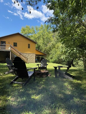 En gul byggnad med en träveranda och ett utomhusområde med sittplatser, inklusive Adirondack-stolar och en eldstad.