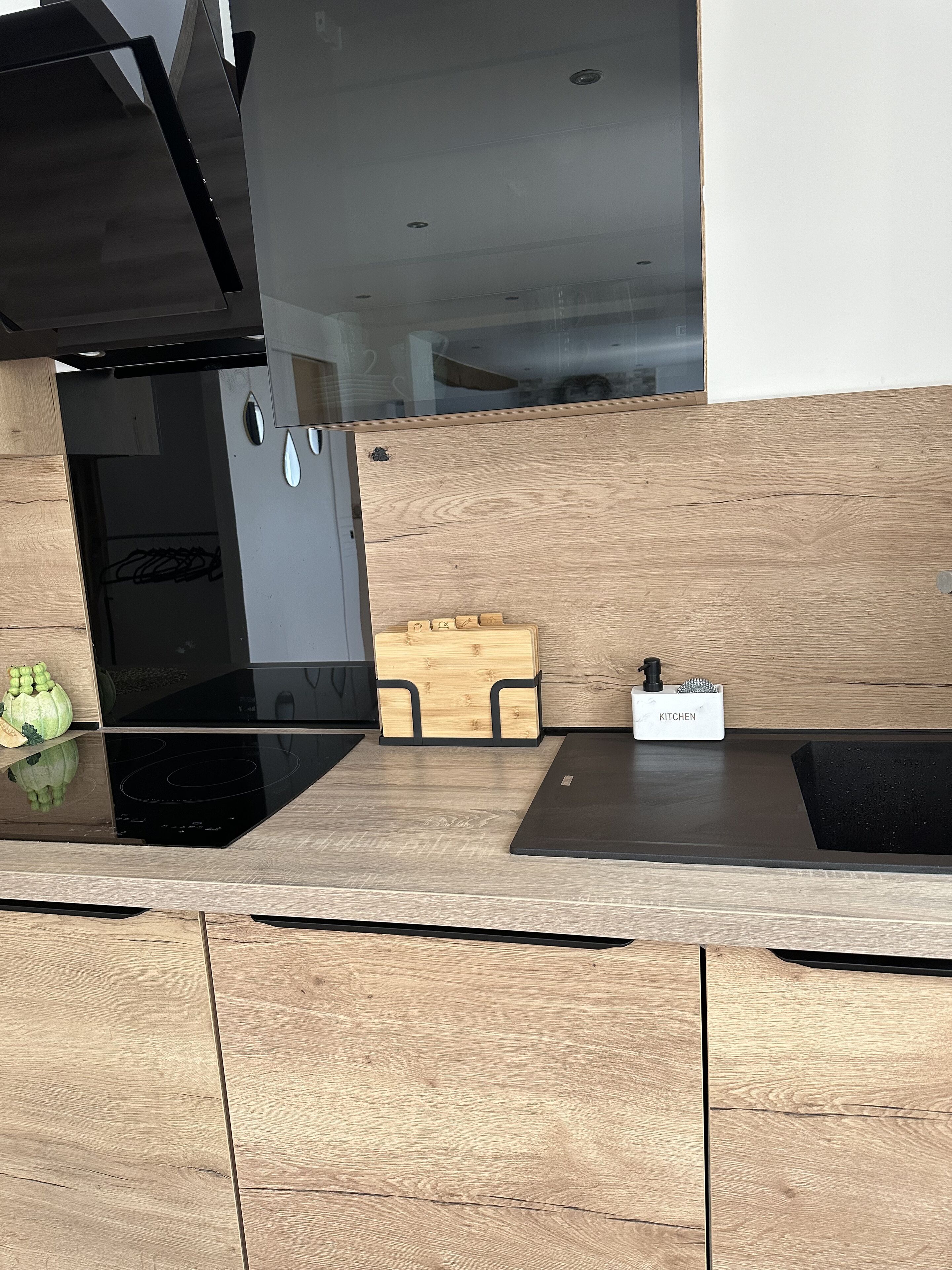 Een moderne keuken met een houten aanrecht, een zwarte kookplaat en een klein keukenapparaat met de tekst 'KITCHEN' op de muur.