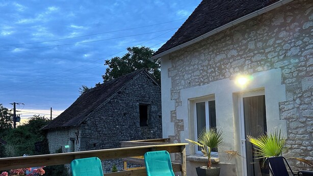Eine Holzterrasse mit zwei türkisfarbenen Liegestühlen und einem Steingebäude im Hintergrund.