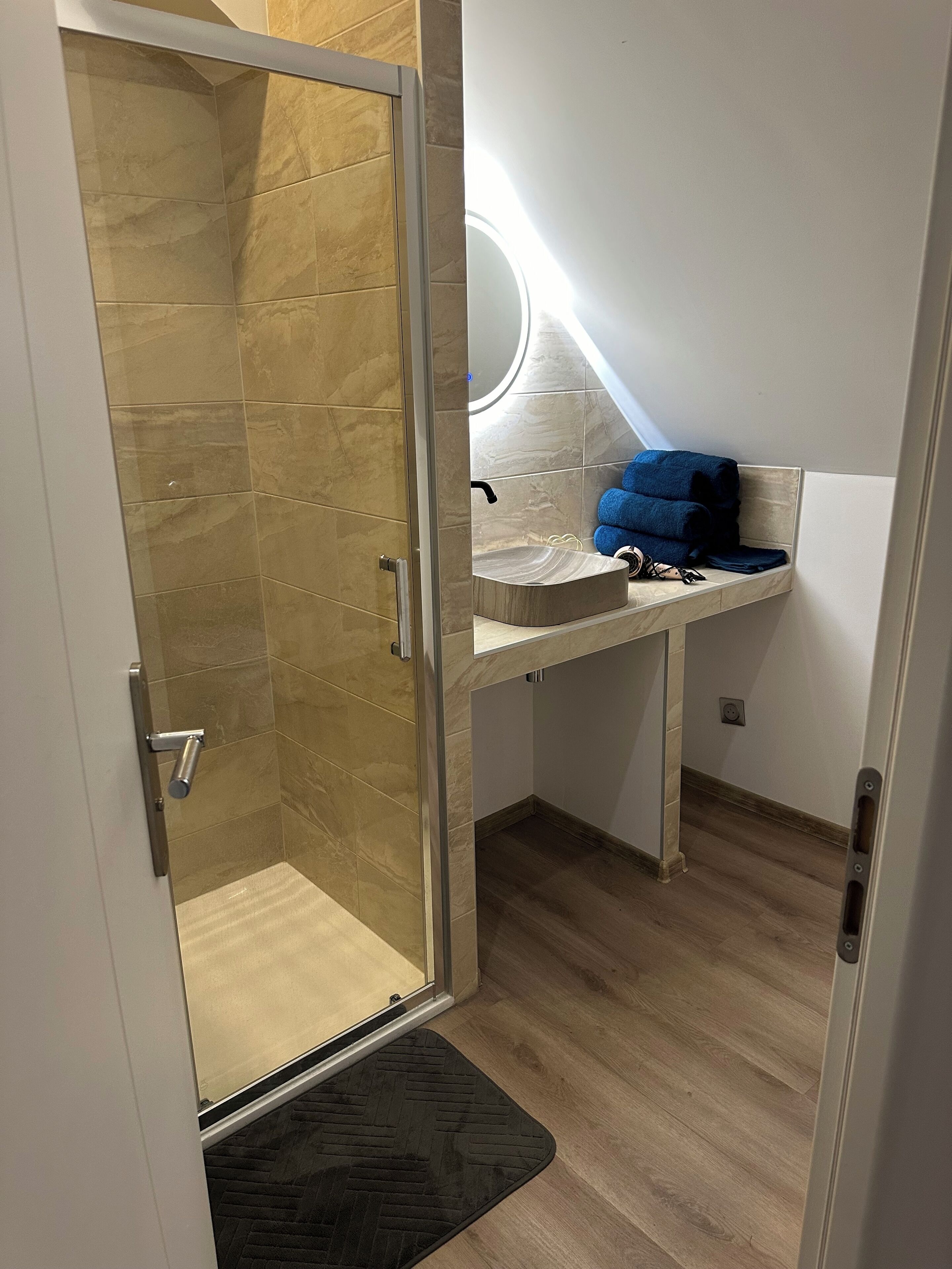Une salle de bain avec une douche à parois de verre, un lavabo avec un miroir et une serviette bleue posée sur le comptoir.