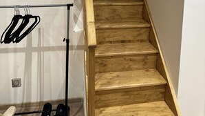 Eine Holztreppe mit Handlauf, ein Metallgestell mit Kleiderbügeln und ein Paar Schuhe am Boden.