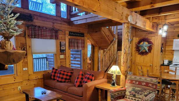 Ein gemütliches Blockhaus-Interieur mit Holzboden, einer Couch, einem gemusterten Sessel, einem Couchtisch und einem Esstisch.