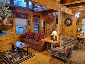 Interior acollidor d'una cabana, amb terra de fusta, un sofà, una butaca amb dibuixos, una taula de cafè i una taula de menjador.