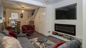 A living room with a sofa, armchair, TV, fireplace, and a staircase leading to another room. - Colliers Cottage (Cinderford)