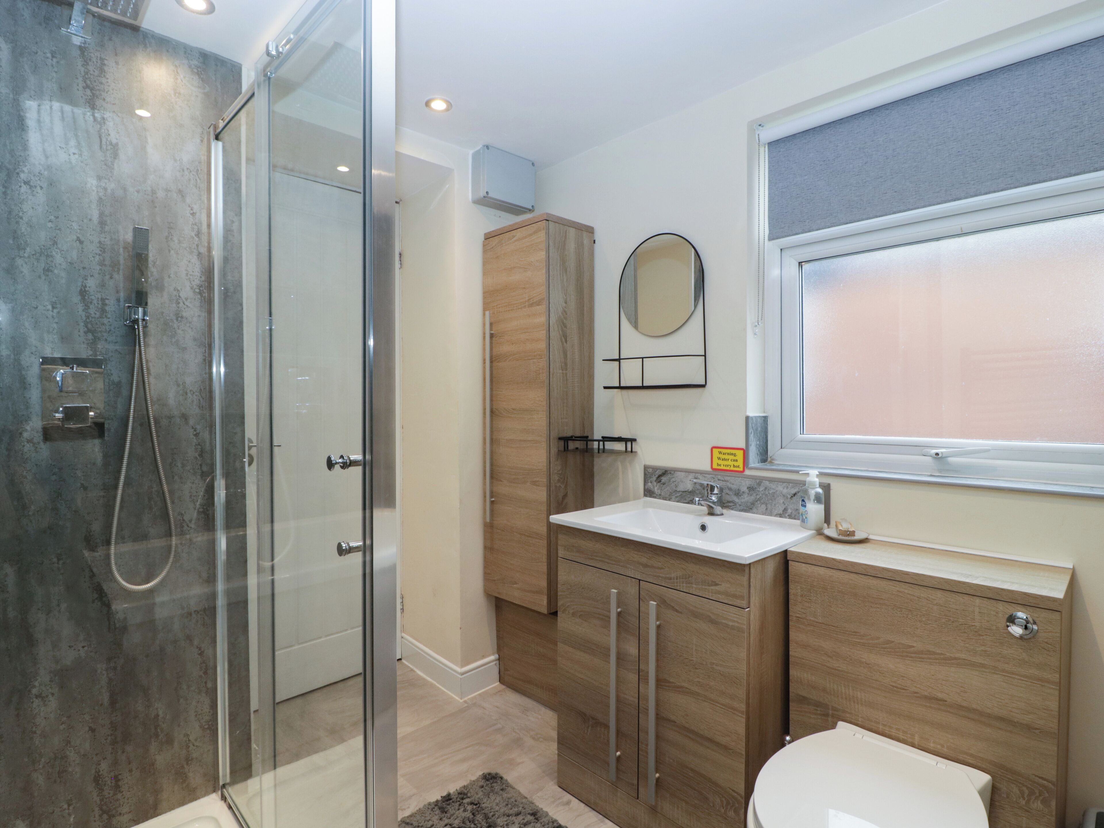 Une salle de bain moderne avec une douche à parois de verre, un meuble-lavabo en bois et un miroir au-dessus du meuble à pharmacie.