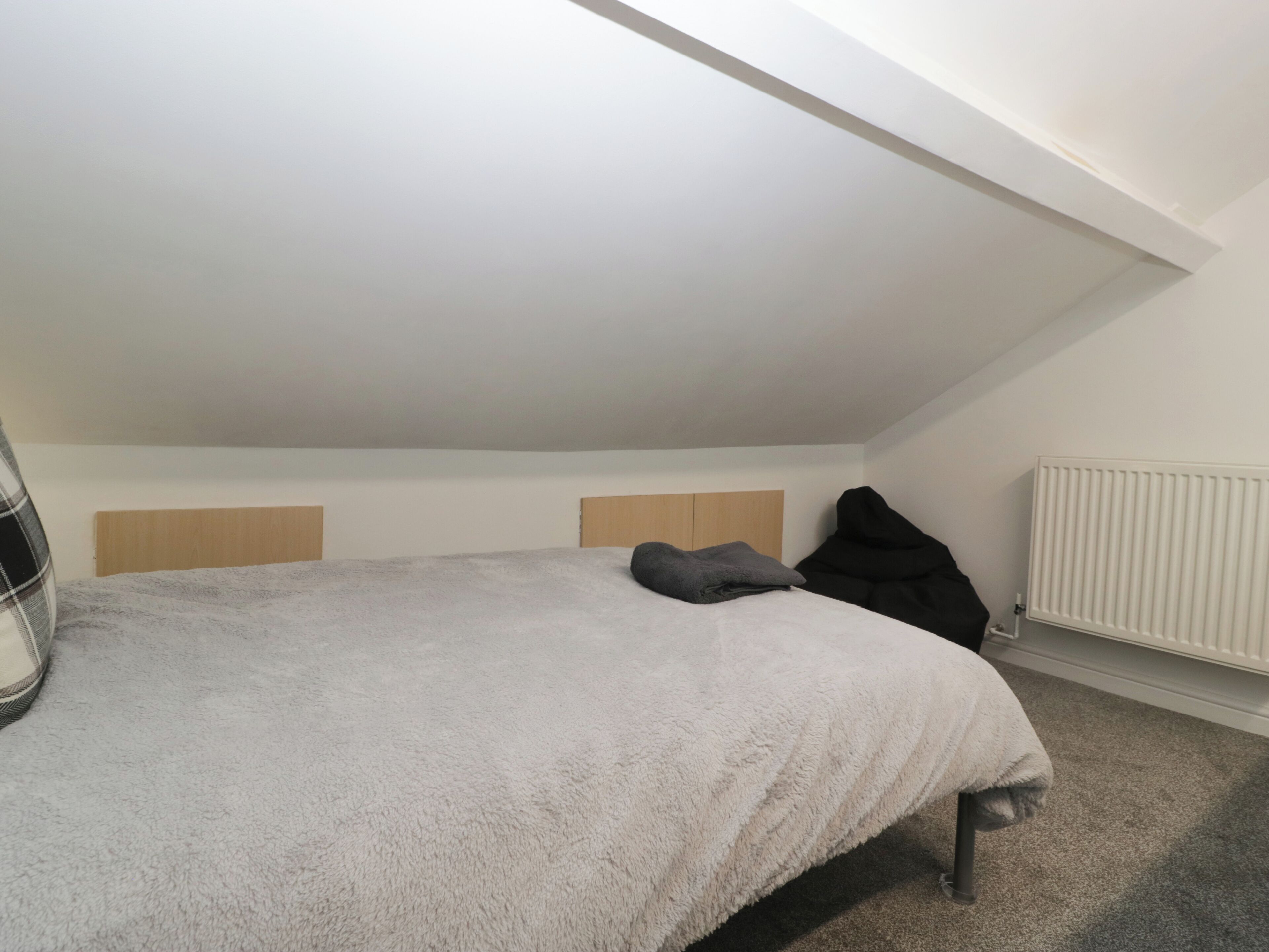 Een slaapkamer met een schuine plafond, een bed met een witte, zachte deken, twee houten hoofdeinden en een radiator.