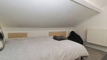 Een slaapkamer met een schuine plafond, een bed met een witte, zachte deken, twee houten hoofdeinden en een radiator.