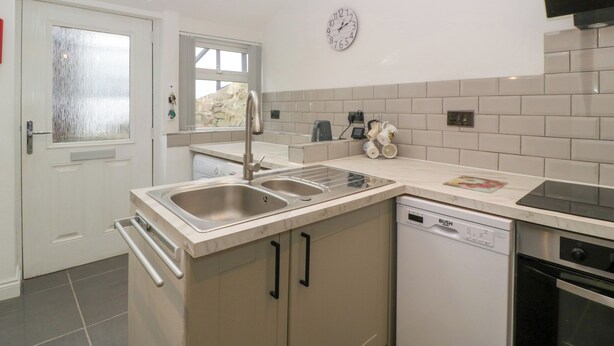 A modern kitchen with a built-in dishwasher, a double sink, and a flat-screen TV mounted on the wall. - Colliers Cottage (Cinderford)