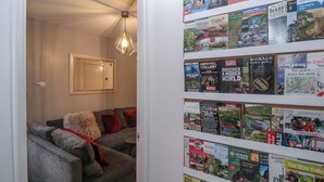 A cozy living room with a grey sofa, a mirror, and a wall-mounted bookshelf filled with travel books. - Colliers Cottage (Cinderford)
