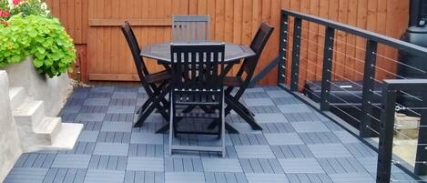 A patio with a table and chairs, a wooden fence, and a metal railing.