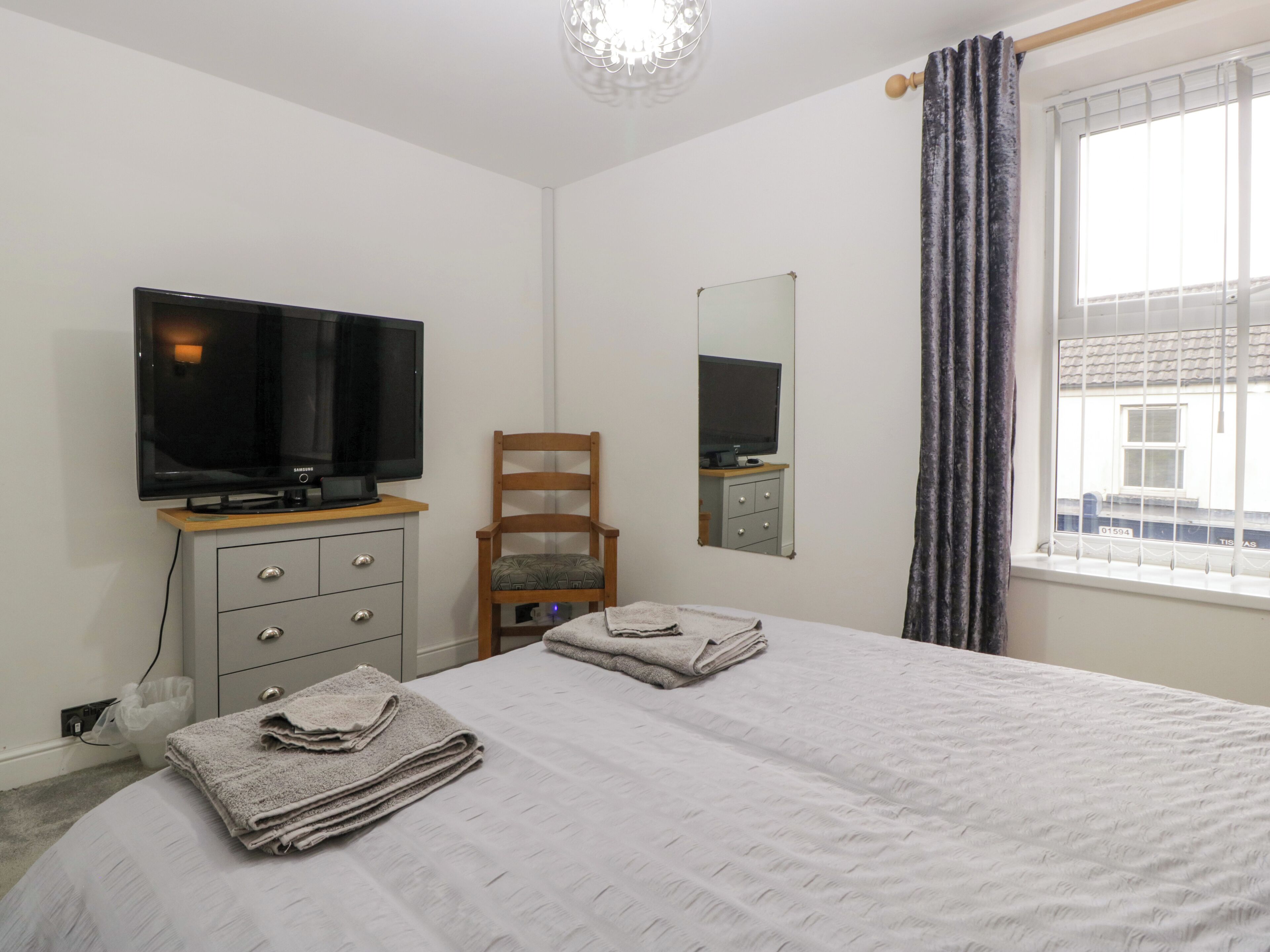 A bedroom with a bed, a TV on a dresser, a chair, and a window with curtains.