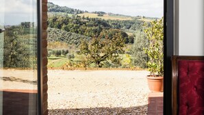 Un balcón accesible con puerta abierta, vistas al paisaje rural, una silla roja y una planta en maceta.
