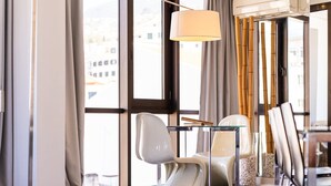 Une chambre d’hôtel moderne avec de grandes fenêtres, une table en verre et des chaises blanches.