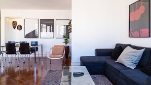 Un salon moderne avec un canapé gris foncé, une table basse en verre et un coin repas comprenant une table et des chaises en verre.