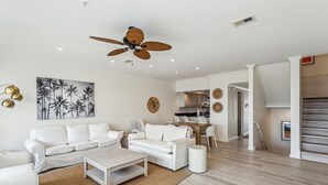 A modern living room with a white sofa set, a coffee table, and a ceiling fan.