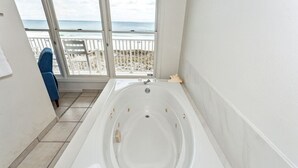 A bathroom with a large bathtub, a window with a view of the beach, and a chair by the window.