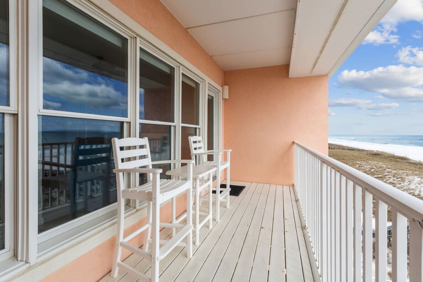 A balcony with white chairs and a table, overlooking a beach.