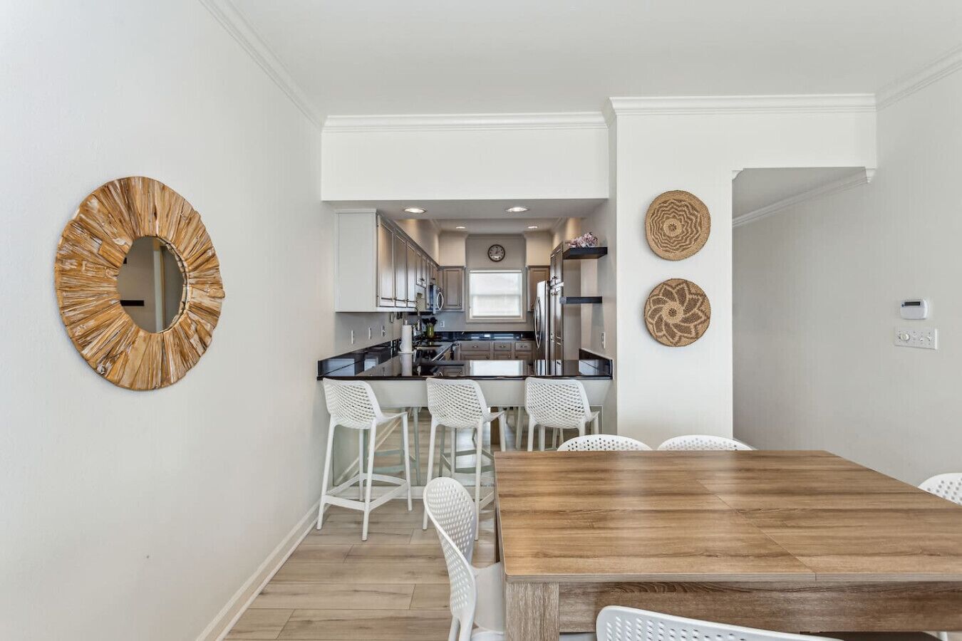 A modern kitchen with white cabinets, a black countertop, and a wooden dining table with white chairs.