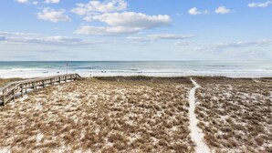 A beach with a wooden boardwalk leading to the shore, sandy dunes, and a clear sky.