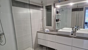 A modern bathroom with a glass-enclosed shower, dual sinks, and a large mirror.