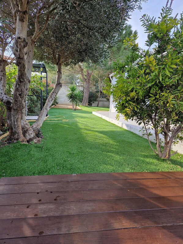 A well-maintained garden with a wooden deck, various trees, and a clear pathway.