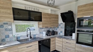 A modern kitchen with wooden cabinets, a black dishwasher, a coffee maker, and a built-in oven.