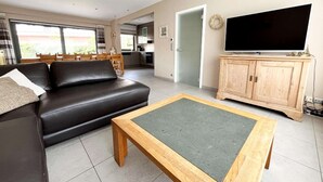 Ein Wohnzimmer mit einer schwarzen Ledersofa, einem Holztisch und einem Fernseher auf einer Holzkommode.