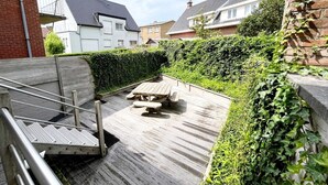 Eine Holzterrasse mit Picknicktisch und Metallgeländern, umgeben von Grünflächen und Wohnhäusern.