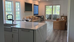 A modern kitchen with a marble island, white cabinetry, and a dining area with a sofa and wicker chair. - Family-friendly Villa by Ocean.  Walk to beach, bike, golf, tennis, fish & pool. (Pawleys Island)