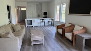 A spacious living area with a sofa, chairs, a coffee table, and a kitchen with white cabinets and a marble backsplash. - Family-friendly Villa by Ocean.  Walk to beach, bike, golf, tennis, fish & pool. (Pawleys Island)