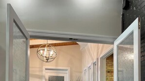 A hallway with frosted glass doors, a black rug, a vase on a pedestal, and a hanging light fixture. - MY PLACE! Luxury 2 Bed with piano! (Willmar)