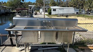 Un barco de metal amarrado en un puerto deportivo, con una plataforma de concreto y una cerca de malla metálica.
